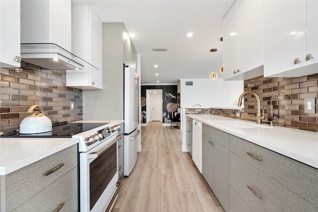 kitchen featuring white appliances, wall chimney range hood, a sink, modern cabinets, and light wood finished floors