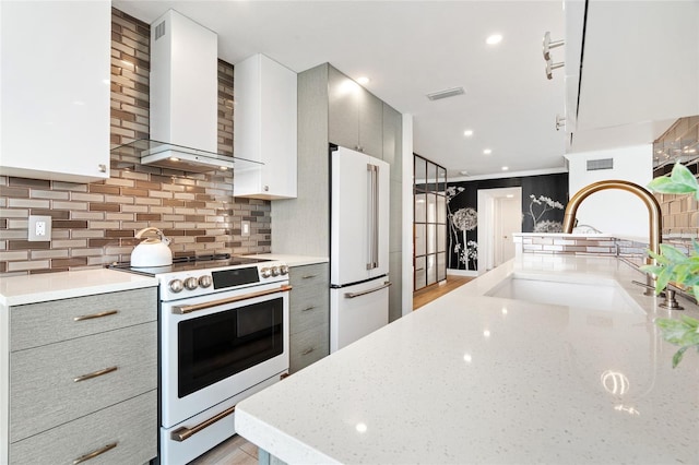kitchen featuring white appliances, wall chimney exhaust hood, a sink, gray cabinetry, and recessed lighting