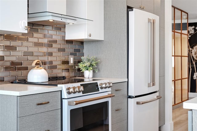 kitchen with white appliances, wall chimney exhaust hood, gray cabinets, and decorative backsplash