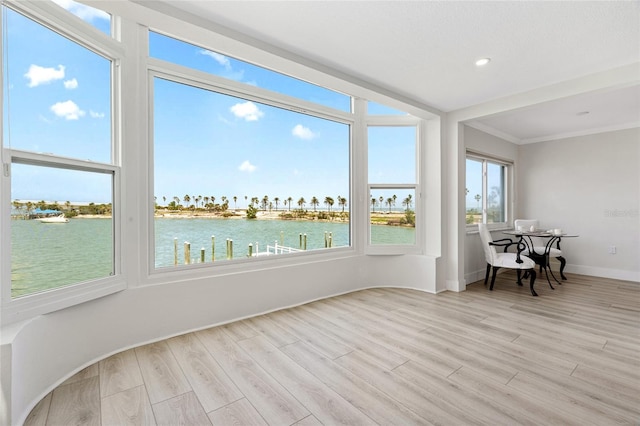 unfurnished sunroom featuring wood finished floors, a water view, ornamental molding, baseboards, and recessed lighting