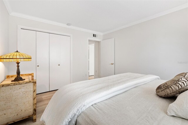bedroom featuring light wood-style floors, ornamental molding, and a closet