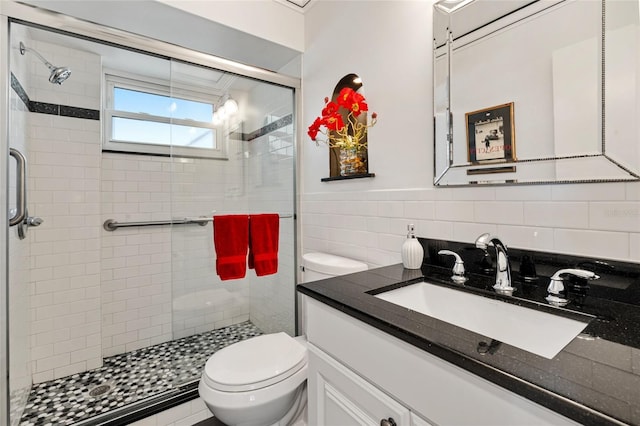 bathroom featuring toilet, a stall shower, vanity, and tile walls