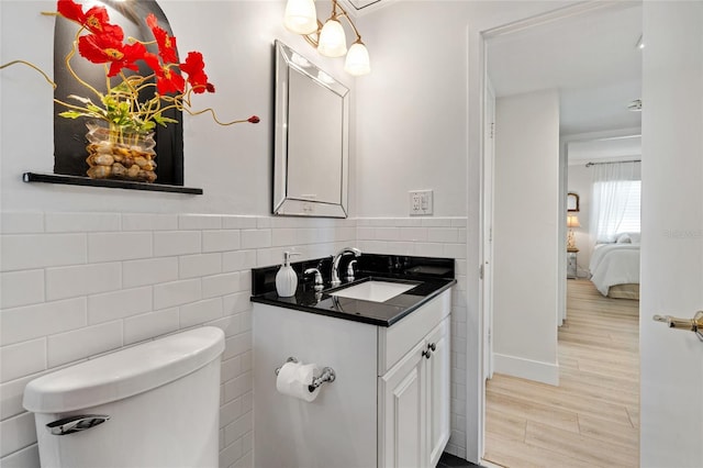 bathroom with vanity, toilet, tile walls, wood finished floors, and baseboards