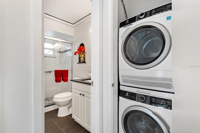 washroom with estacked washer and dryer, dark tile patterned floors, and tile walls