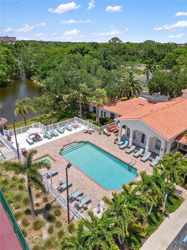 community pool featuring a fenced backyard, a water view, a patio area, and a forest view