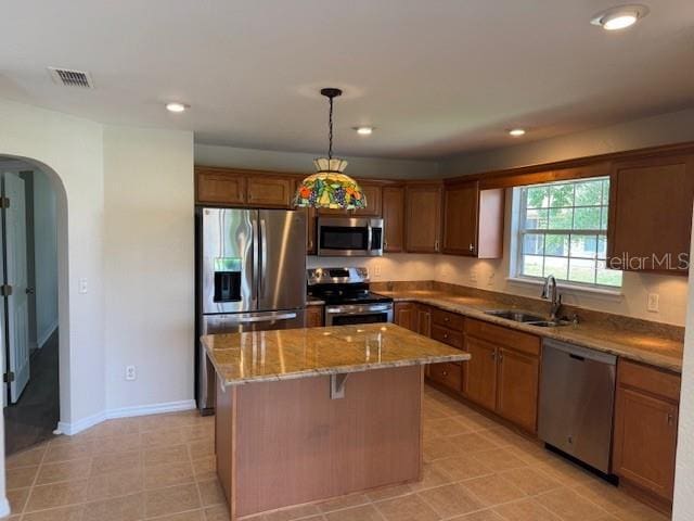 kitchen featuring stainless steel appliances, a sink, arched walkways, a kitchen island, and stone counters