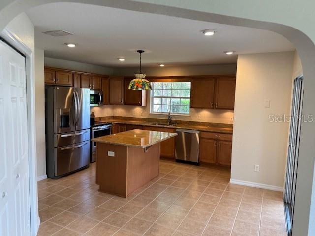 kitchen with appliances with stainless steel finishes, arched walkways, a kitchen island, light tile patterned floors, and recessed lighting