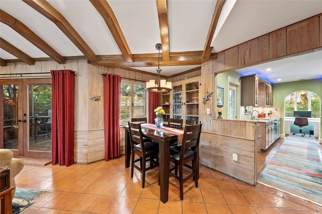 941 Virginia Dr, Sarasota, FL 34234 - dining space featuring a chandelier, beamed ceiling, wood walls, french doors, and light tile patterned flooring