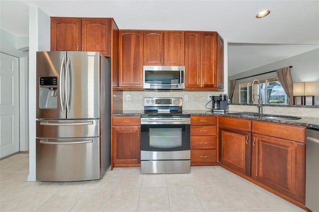 kitchen featuring appliances with stainless steel finishes, a sink, dark stone countertops, tasteful backsplash, and light tile patterned flooring