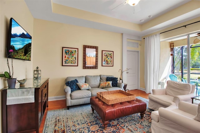 living room featuring wood finished floors, baseboards, a ceiling fan, and a raised ceiling