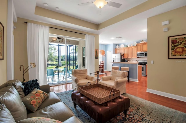 living area featuring a ceiling fan, light wood-type flooring, and baseboards