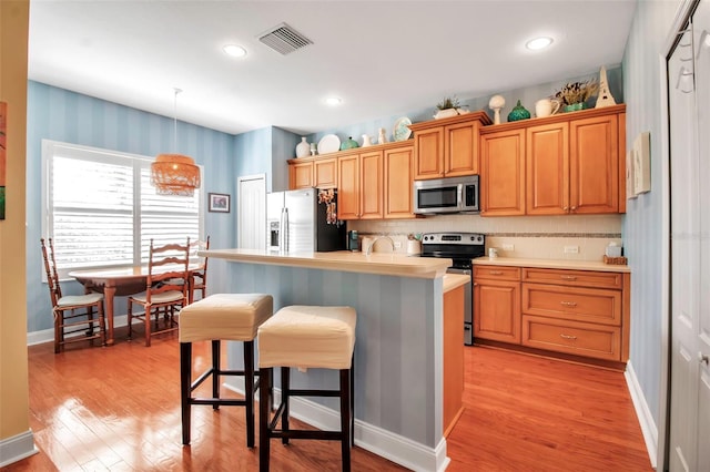 kitchen with appliances with stainless steel finishes, a breakfast bar, light countertops, light wood-style flooring, and a kitchen island