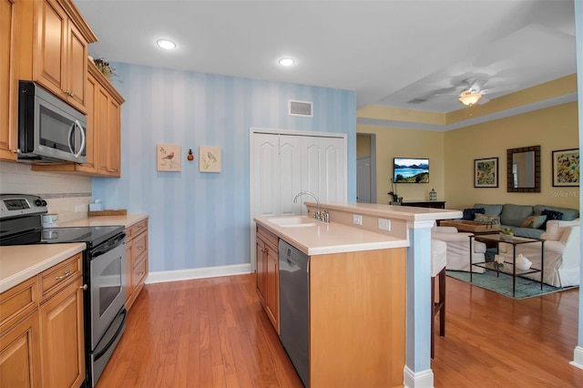 kitchen featuring stainless steel appliances, a sink, a kitchen bar, wallpapered walls, and light wood finished floors