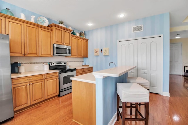 kitchen with stainless steel appliances, a breakfast bar, light countertops, light wood-style flooring, and a center island with sink