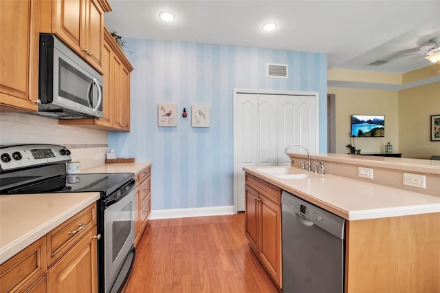 kitchen featuring stainless steel appliances, a sink, wallpapered walls, baseboards, and light countertops