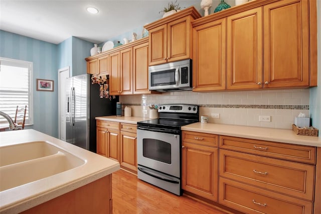 kitchen with stainless steel appliances, a sink, wallpapered walls, light wood-style floors, and light countertops