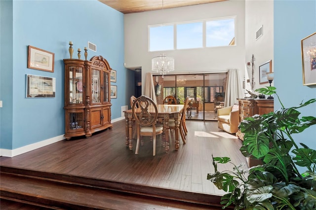 dining room with a towering ceiling, a chandelier, wood-type flooring, healthy amount of natural light, and baseboards