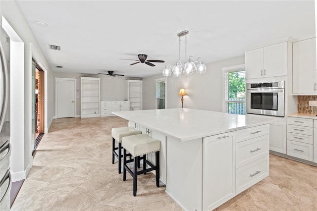 911 Cimarron Cir, Bradenton, FL 34209 - kitchen featuring oven, a kitchen island, light countertops, ceiling fan, and white cabinetry