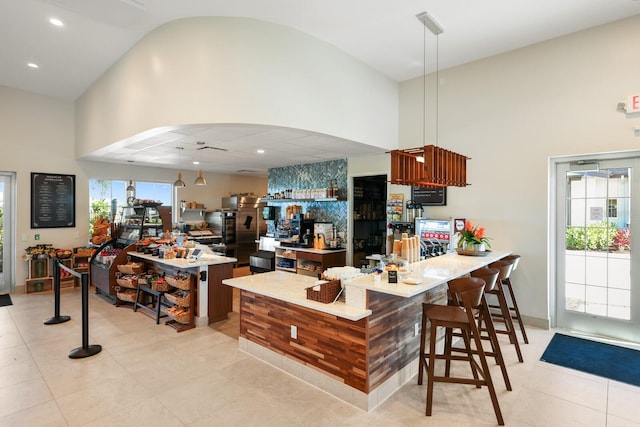 kitchen featuring high vaulted ceiling, arched walkways, light tile patterned floors, a peninsula, and a breakfast bar area