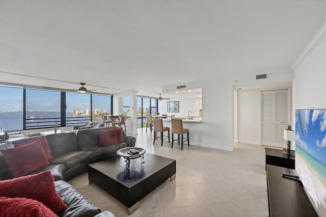 living room featuring light tile patterned floors, a ceiling fan, a wall of windows, baseboards, and a water view