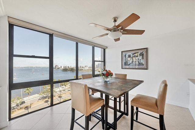 dining space featuring a water view, a wall of windows, light tile patterned flooring, and a ceiling fan
