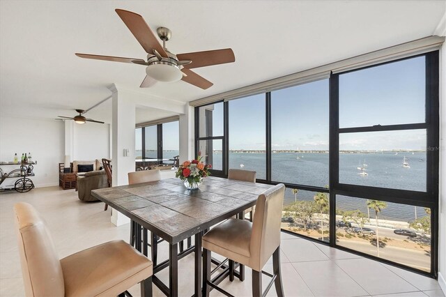 dining room featuring a wall of windows, a water view, healthy amount of natural light, ceiling fan, and light tile patterned flooring