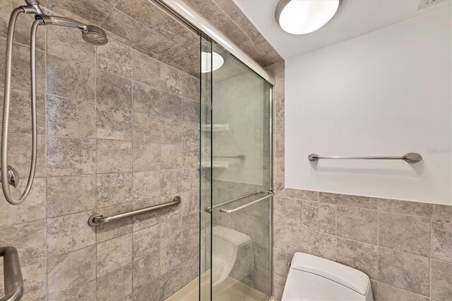 full bathroom with toilet, a shower stall, tile walls, and a wainscoted wall