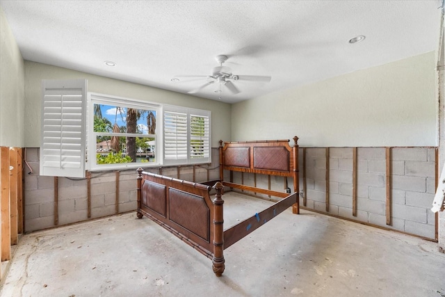 bedroom featuring unfinished concrete floors, a textured ceiling, concrete block wall, and ceiling fan