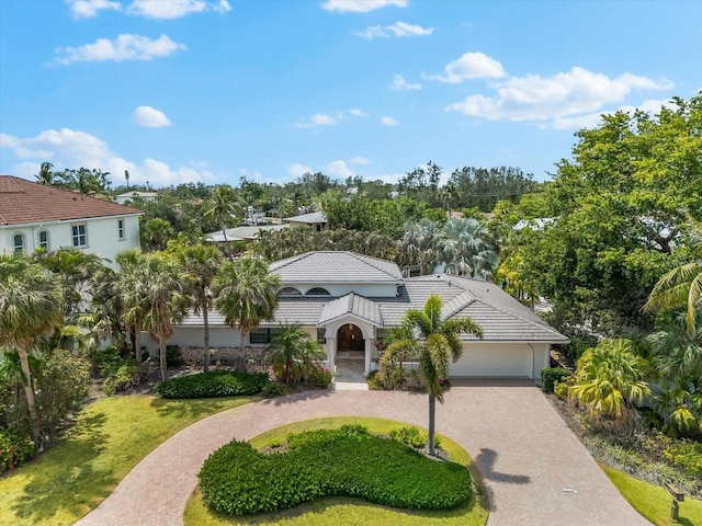 mediterranean / spanish home featuring curved driveway, a tile roof, view of scattered trees, and stucco siding