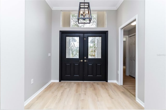 foyer entrance with a chandelier, light wood-type flooring, baseboards, and crown molding
