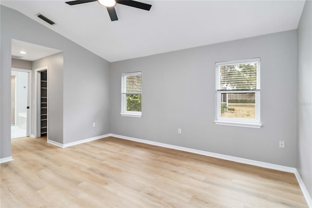 empty room with plenty of natural light, a ceiling fan, light wood-type flooring, lofted ceiling, and baseboards
