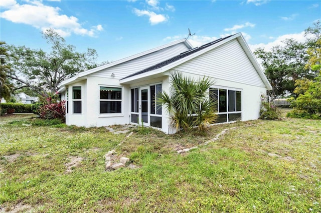 rear view of property featuring a lawn, a sunroom, and stucco siding