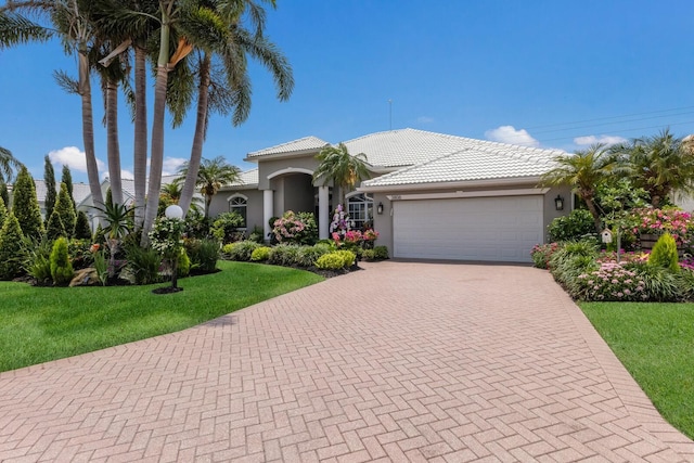 3806 72nd Ter E, Sarasota, FL 34243 - mediterranean / spanish-style home featuring decorative driveway, stucco siding, an attached garage, a front lawn, and a tile roof
