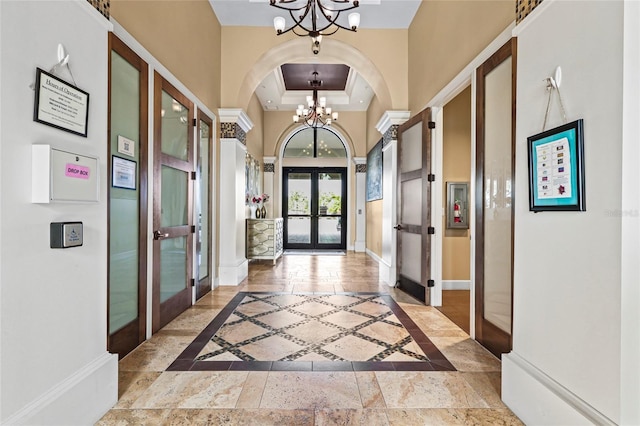 foyer featuring french doors, a chandelier, inlaid floor details, baseboards, and a tray ceiling
