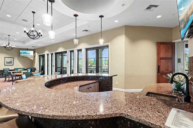 kitchen featuring a sink, a tray ceiling, recessed lighting, stone countertops, and hanging light fixtures
