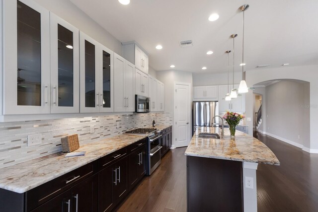 8191 Gabanna Dr, Sarasota, FL 34231 - kitchen with appliances with stainless steel finishes, a sink, arched walkways, white cabinetry, and an island with sink