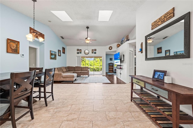 living room with a ceiling fan, lofted ceiling, a skylight, and a textured ceiling