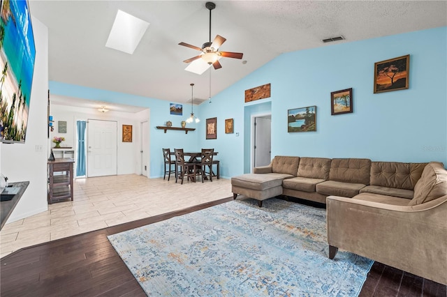 living area with wood finished floors, ceiling fan, vaulted ceiling, and a skylight