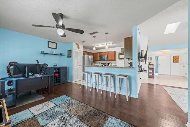 living room featuring wood finished floors, ceiling fan, a textured ceiling, and a skylight