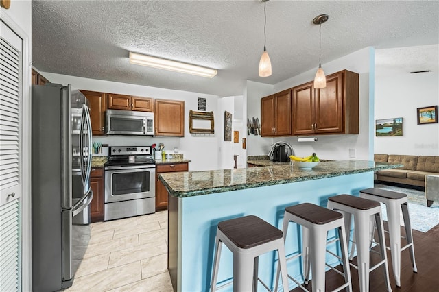 kitchen with stainless steel appliances, a peninsula, a breakfast bar, hanging light fixtures, and dark stone counters