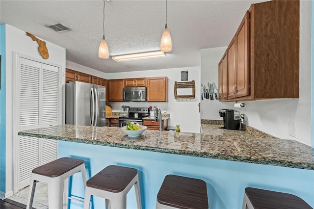 kitchen with stainless steel appliances, a peninsula, a breakfast bar area, decorative light fixtures, and dark stone counters