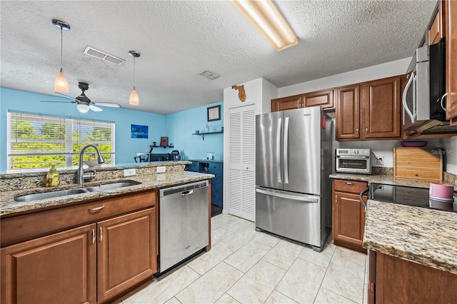 kitchen with appliances with stainless steel finishes, a sink, ceiling fan, pendant lighting, and light stone countertops