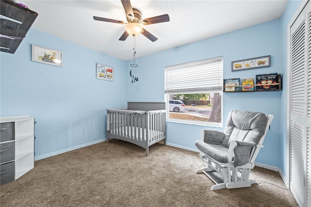 carpeted bedroom featuring a closet, baseboards, a crib, and a ceiling fan