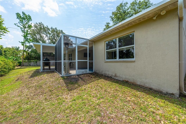 back of house with stucco siding, a lawn, glass enclosure, and a patio