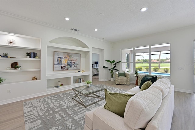 living room featuring a textured ceiling, light wood-style flooring, ornamental molding, built in shelves, and baseboards