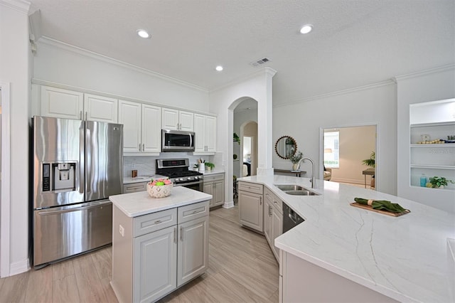 kitchen featuring stainless steel appliances, a sink, a kitchen island, arched walkways, and ornamental molding