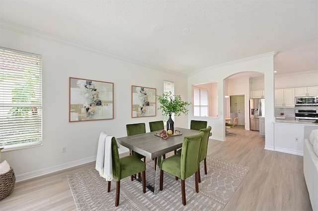 dining room with arched walkways, ornamental molding, light wood finished floors, plenty of natural light, and a textured ceiling