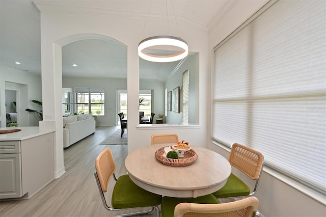 dining area featuring crown molding, light wood-style floors, vaulted ceiling, arched walkways, and baseboards