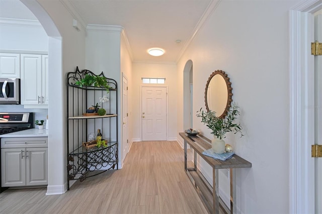 doorway featuring light wood-type flooring, arched walkways, baseboards, and crown molding