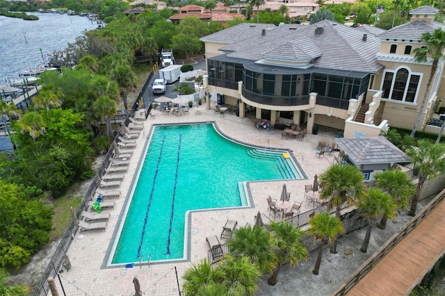 community pool with stairs, a sunroom, a patio, and a water view